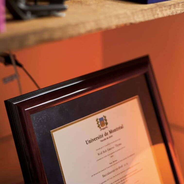 On aperçoit quelques-uns des diplômes et des prix reçus par Wolf Thyma au milieu des ouvrages de droit, de psychiatrie, de recettes de cuisine et de poésie haïtienne.