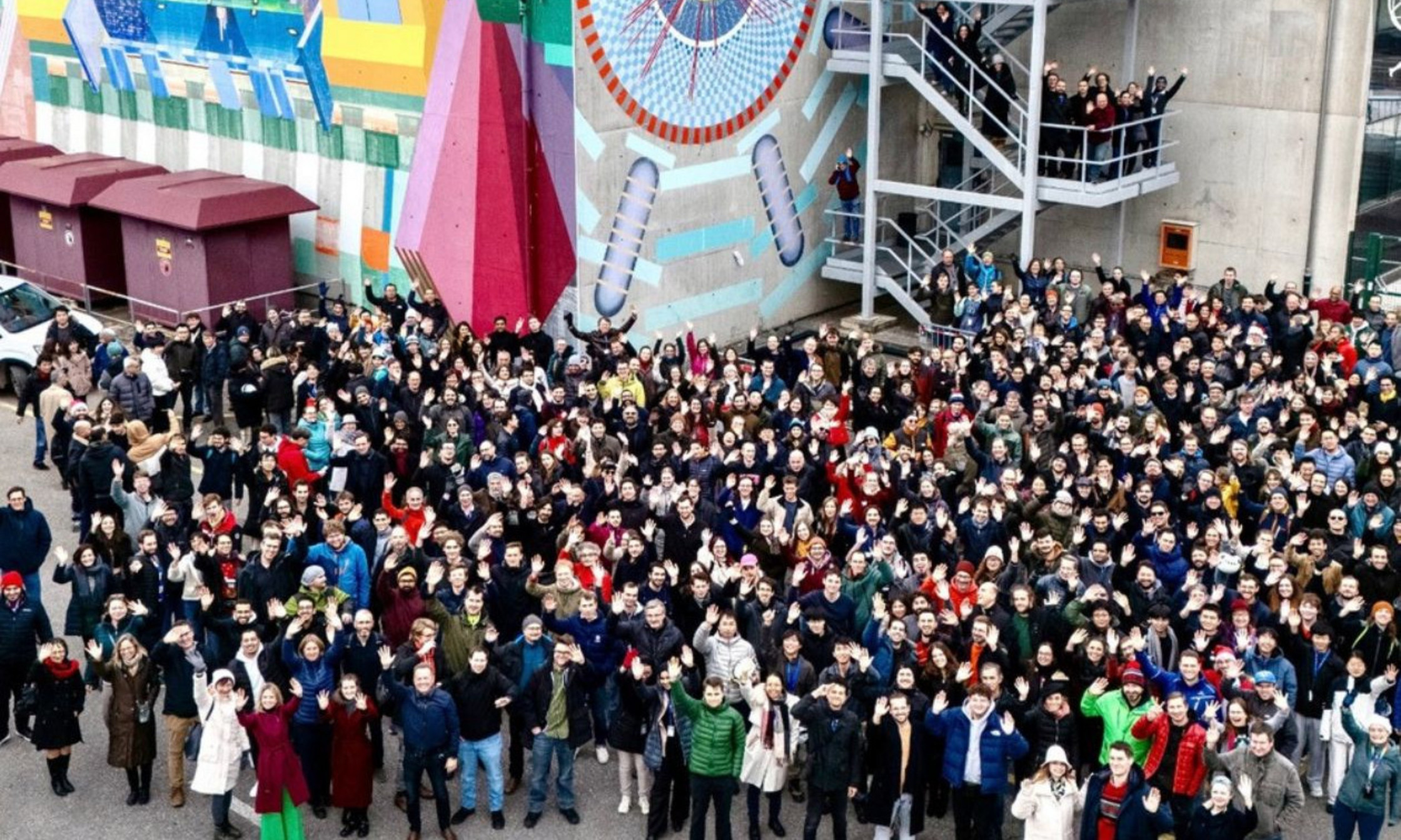 Membres du project ATLAS devant une fresque murale du détecteur ATLAS, au CERN, à la frontière franco-suisse.