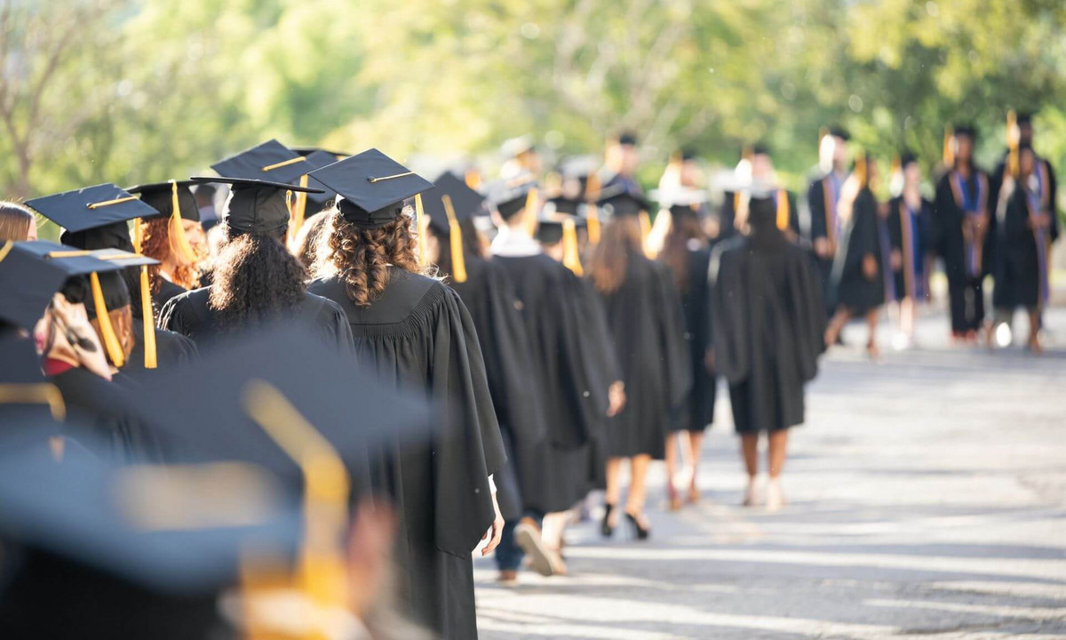 Des diplômés en toge et mortier marchent.